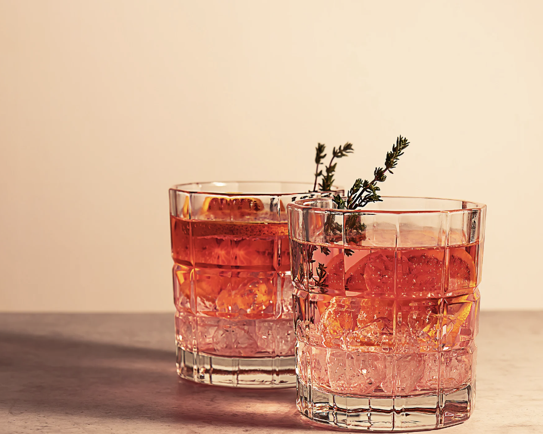 Two whiskey cocktails with rosemary garnish sitting on a table.