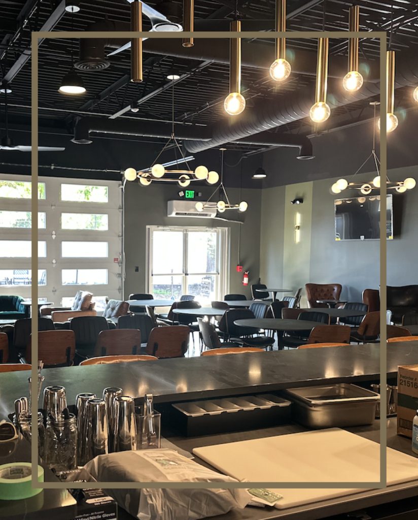 Wide shot of the Highline Spirit's Dexter Tasting Room. With low hanging light fixtures and a mix of wooden and leather seating.