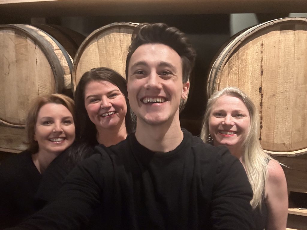 One man and three women standing in front of whiskey barrels